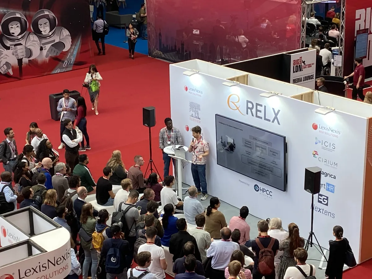 Aerial view of Adrian presenting Scopus AI at the RELX booth during AI London conference, with a large crowd gathered around the stage