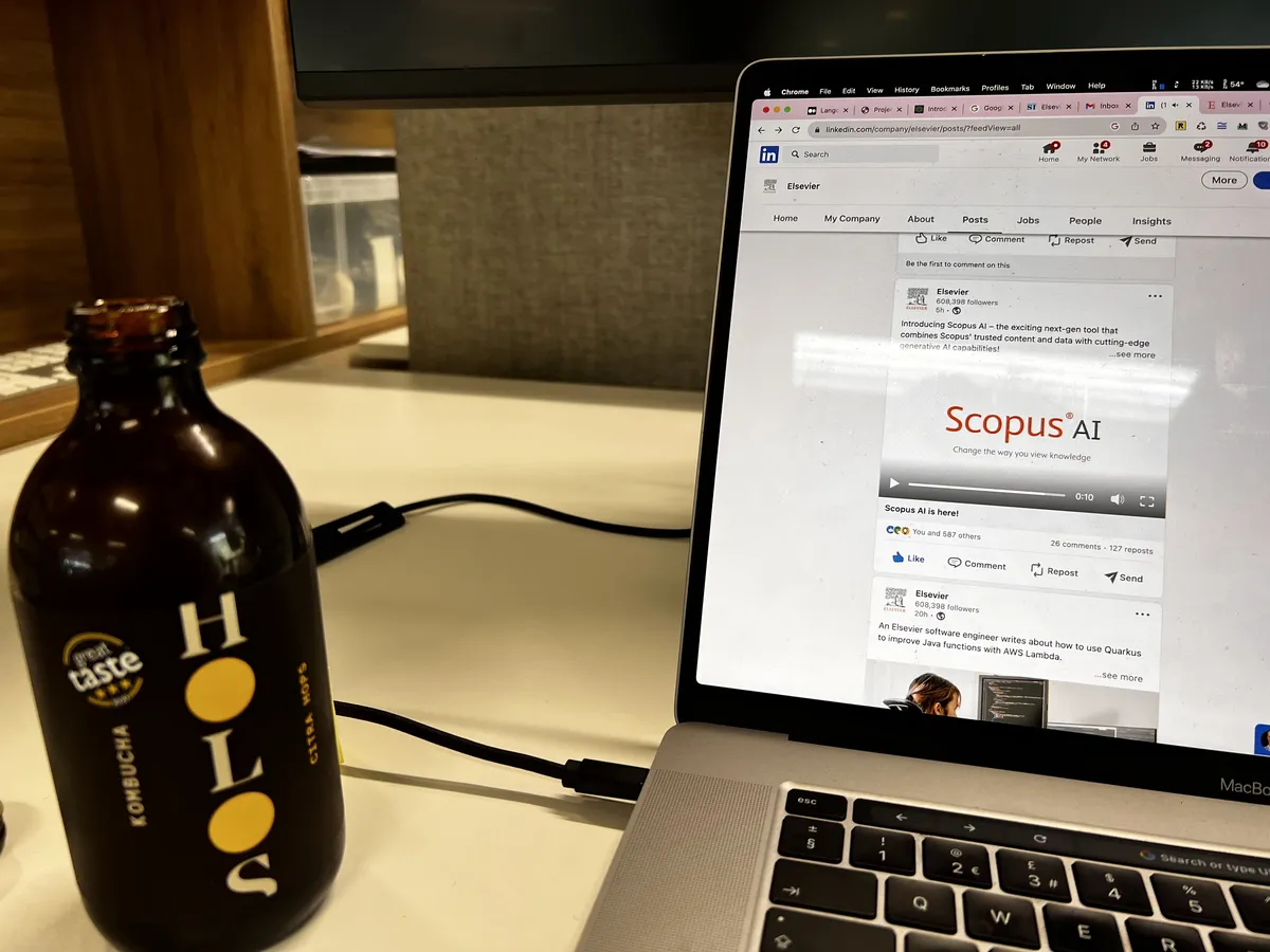 Laptop showing the Elsevier LinkedIn post announcing Scopus AI is here, with a bottle of Holos kombucha beside it