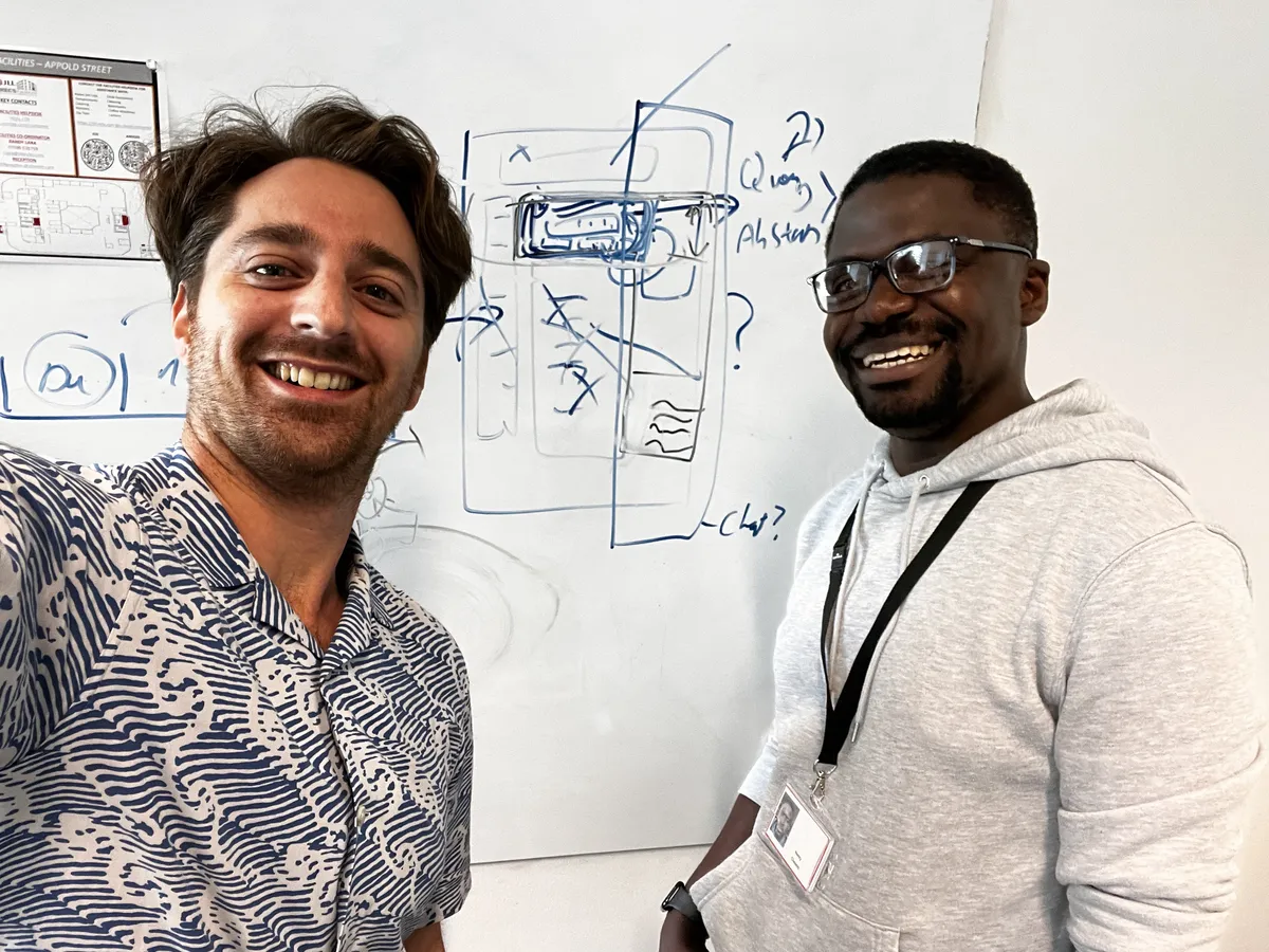 Adrian and Henry smiling in front of a whiteboard covered in UI wireframe sketches for the Scopus AI prototype